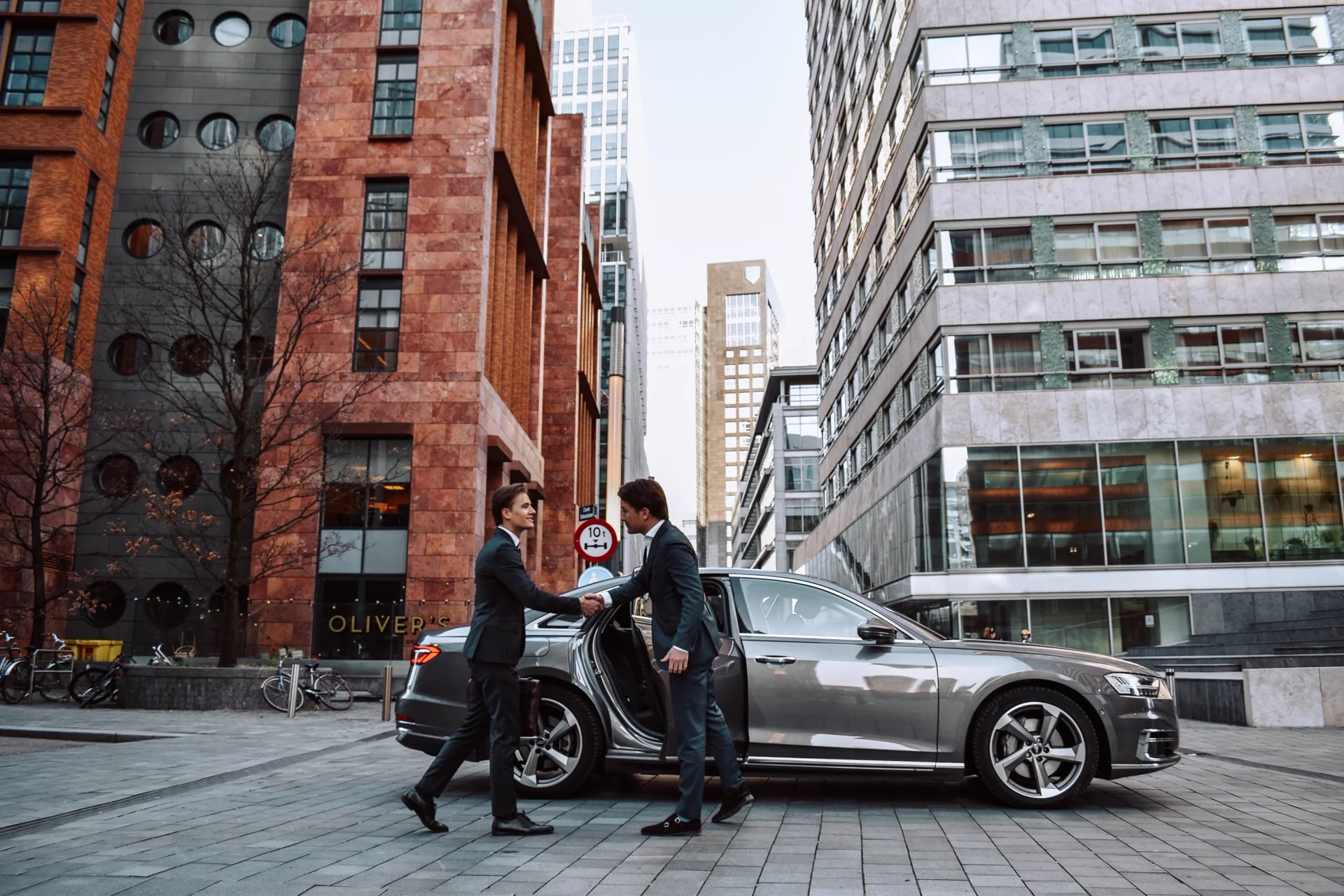 Jonge privéchauffeur ontvangt een zakelijke gast naast de auto
